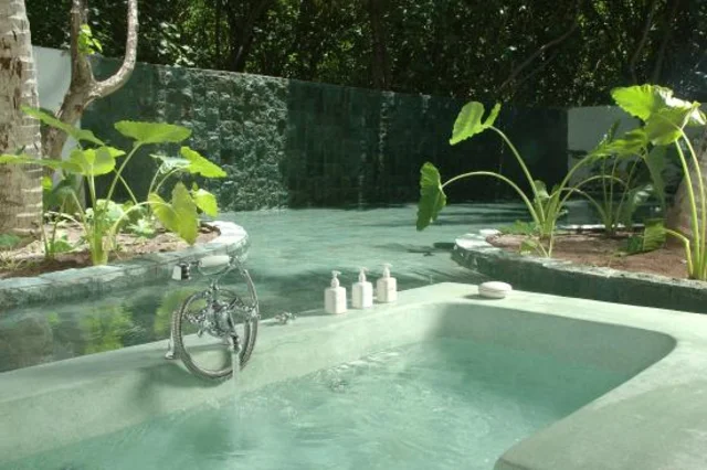 Imagem de banheira verde, ao lado de piscina, completamente ao ar livre.