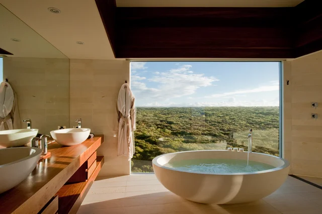 Imagem de banheira de granito em frente a janela enorme, que toma metade da parede do banheiro.